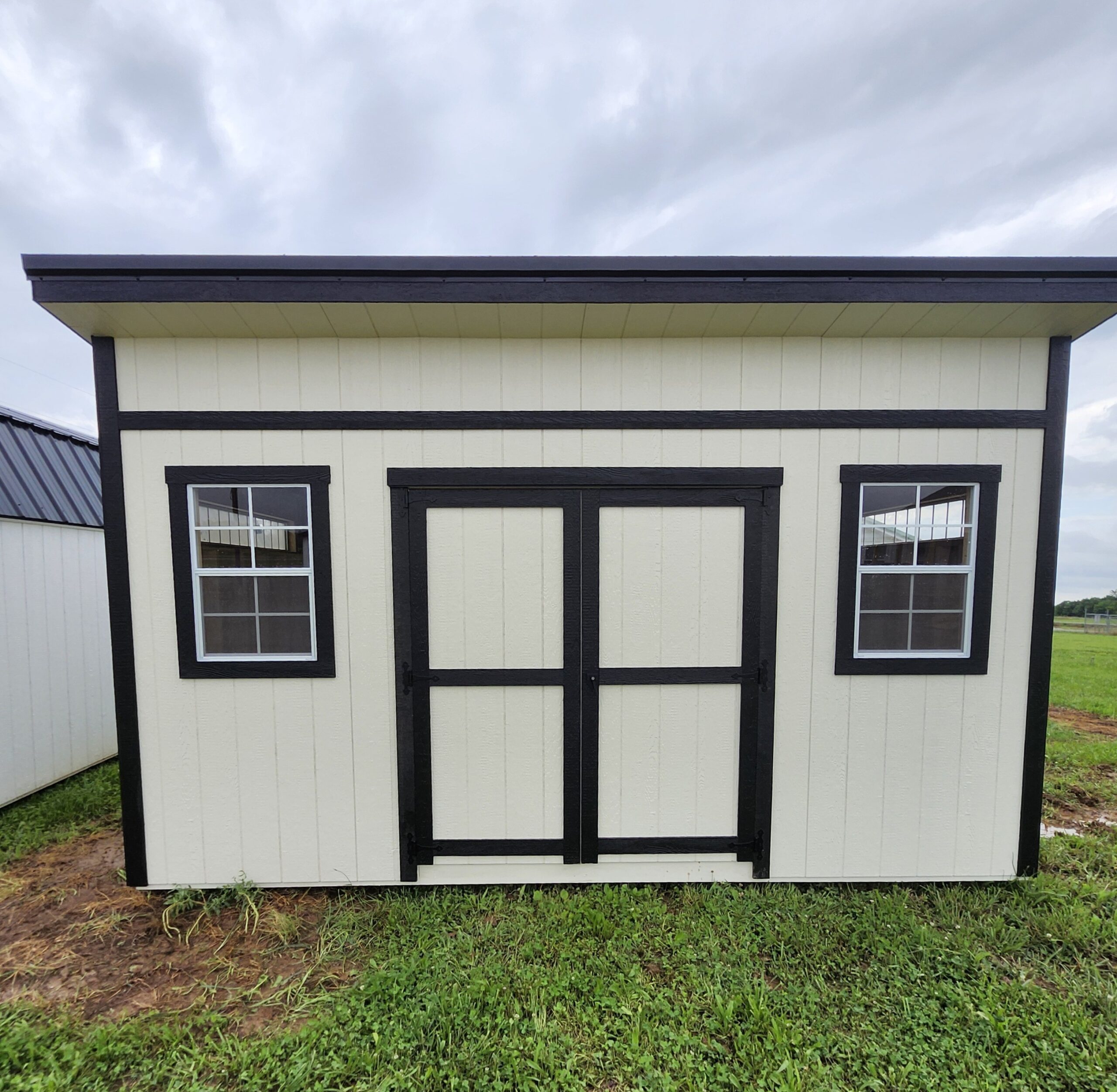 Front view of a beige building with black trim, two windows, and a centered door under a cloudy sky.