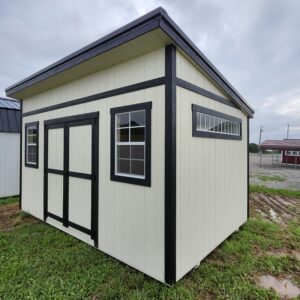 Small cream-colored shed with black trim and two windows, set on a grassy lot under a cloudy sky (corner view).