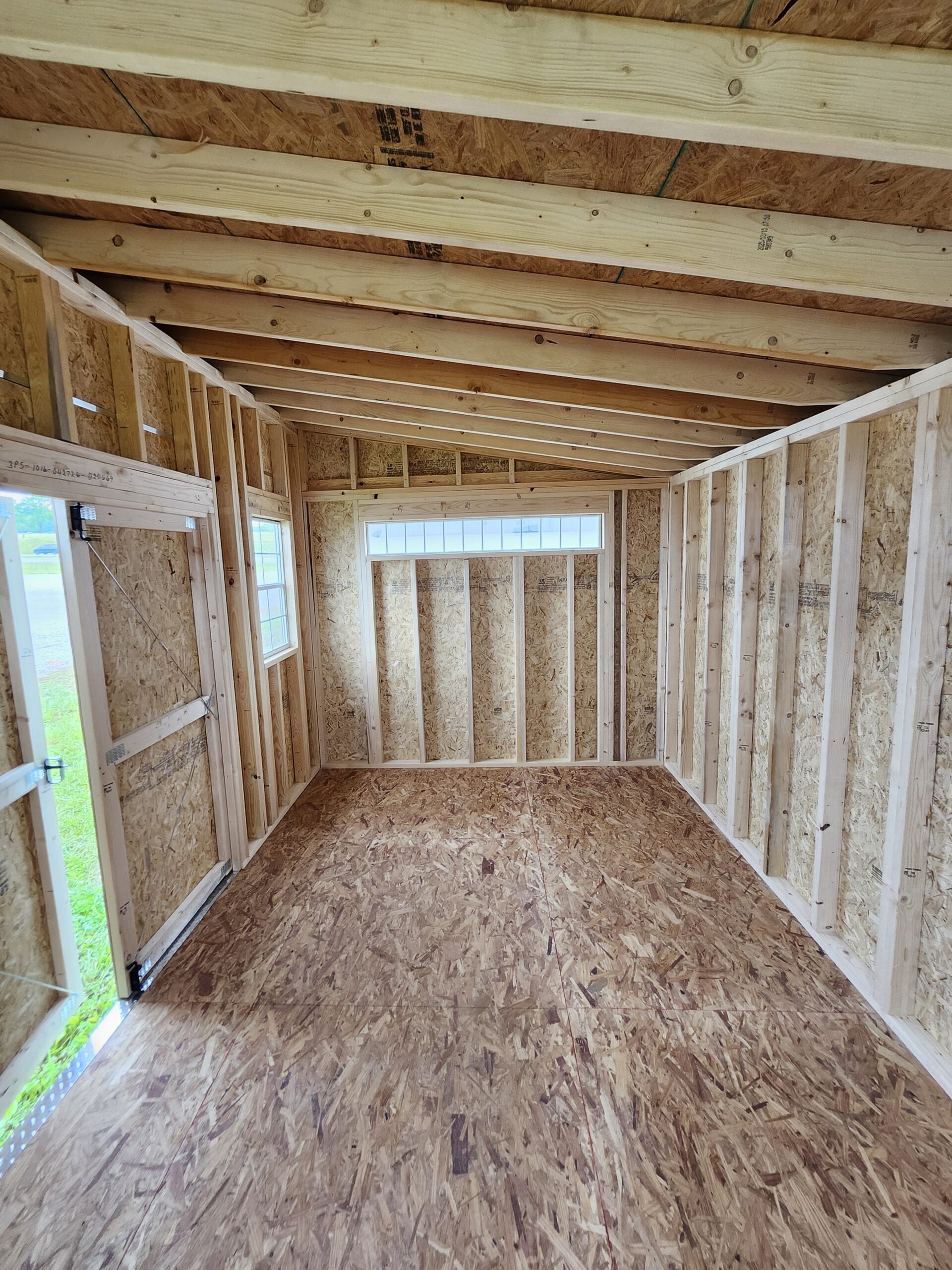 Interior of a framing stage: exposed studs, OSB walls, and angled roof rafters with a window at the far end
