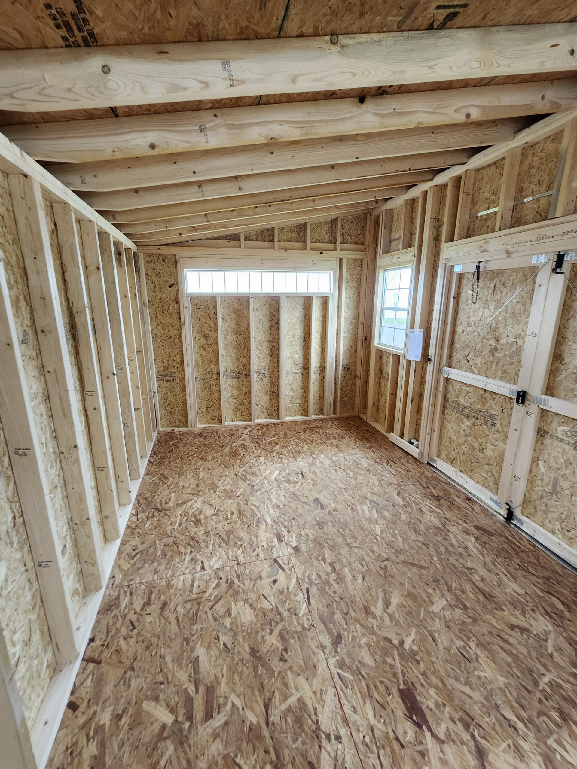 Unfinished room with exposed wooden studs, OSB walls and ceiling, and a small window at the far wall.