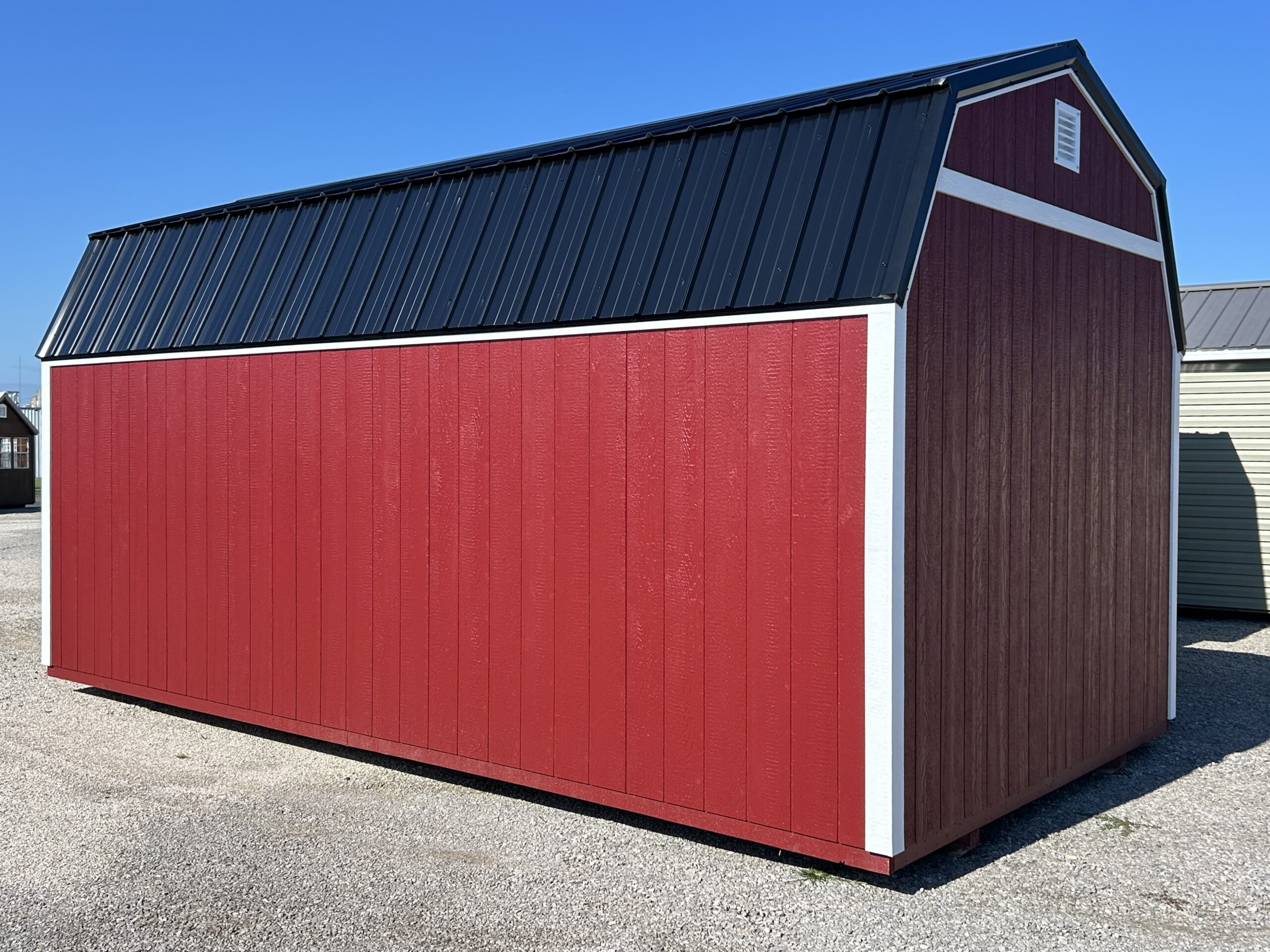 Red barn-style shed with a dark metal sloped roof and white trim against a clear blue sky.