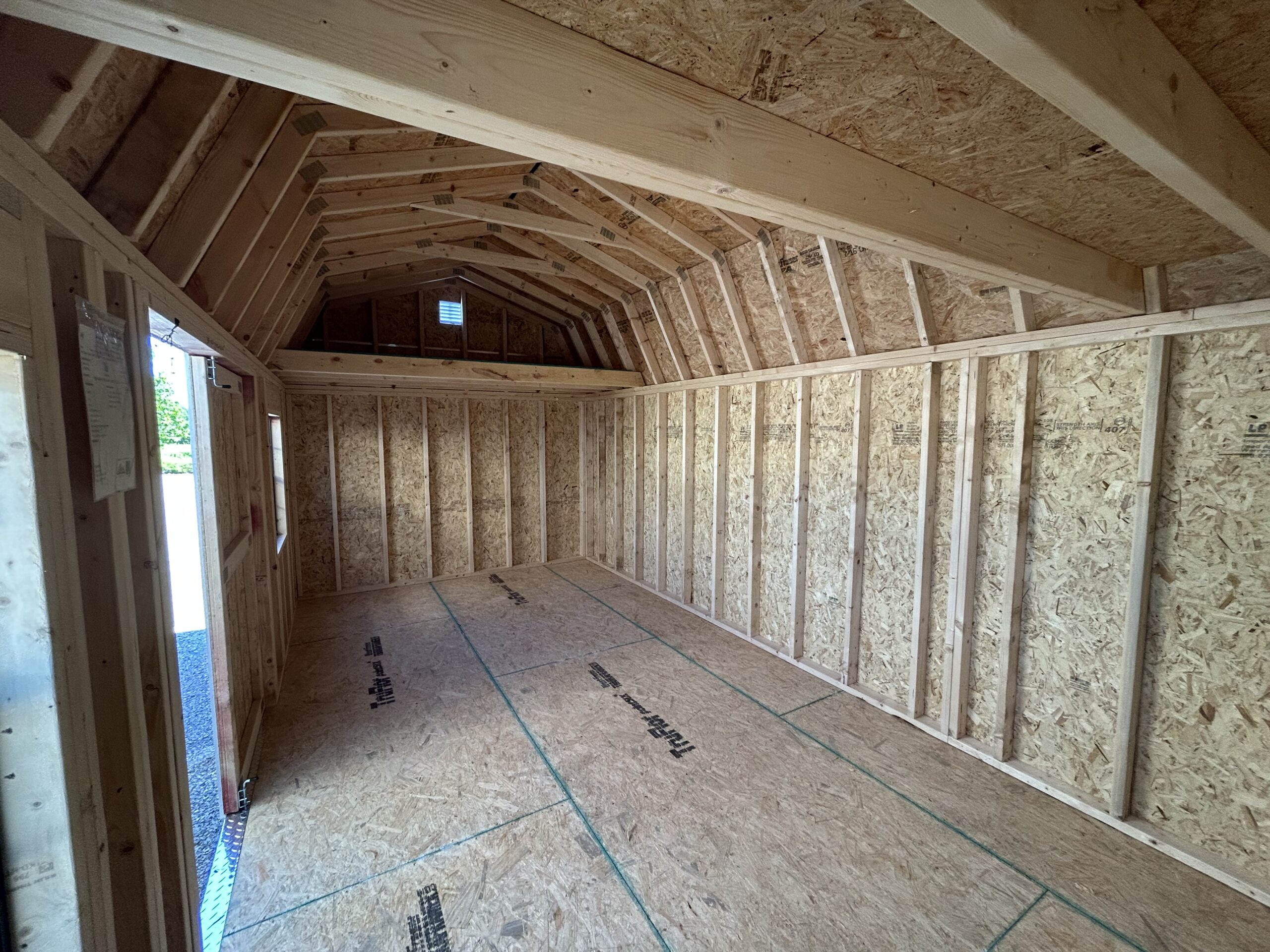 Unfinished attic space with exposed wooden studs, OSB walls, and pitched roof trusses