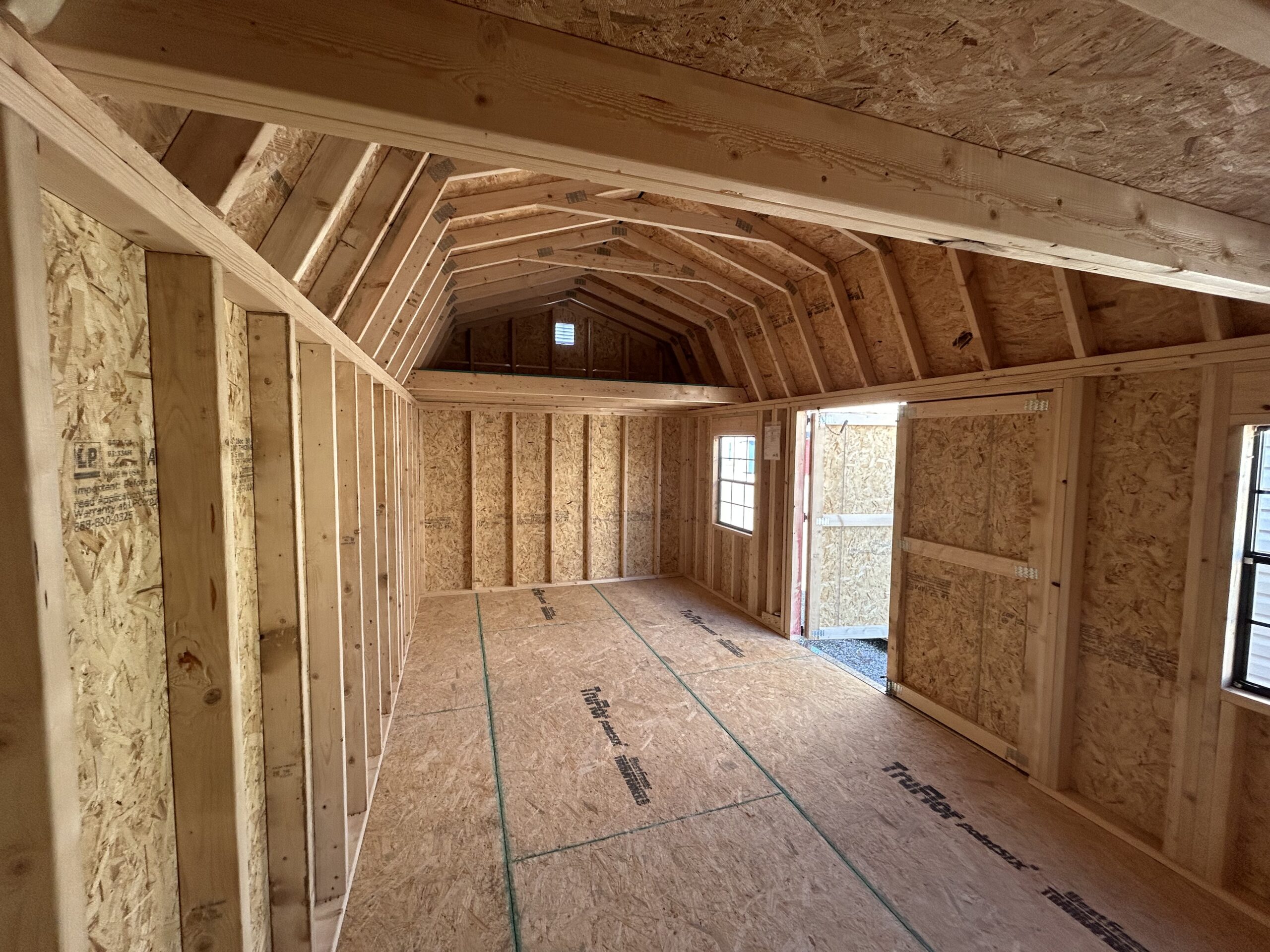 Interior of a framed unfinished attic with exposed wooden studs, roof trusses, and OSB walls and ceiling.