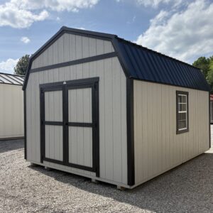 Grey storage shed with black trim, blue metal gabled roof, on gravel under a partly cloudy sky.