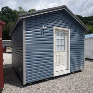 Blue metal siding storage shed with a white framed door and window on a gravel lot under a cloudy sky.