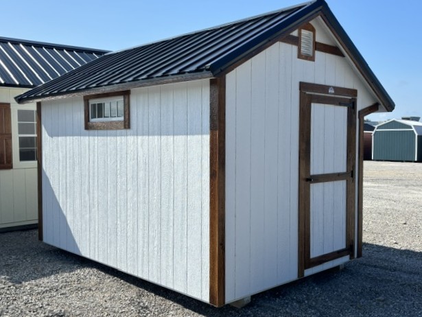 White storage shed with brown trim and a metal sloped roof, on a gravel lot with a small window and a large front door.