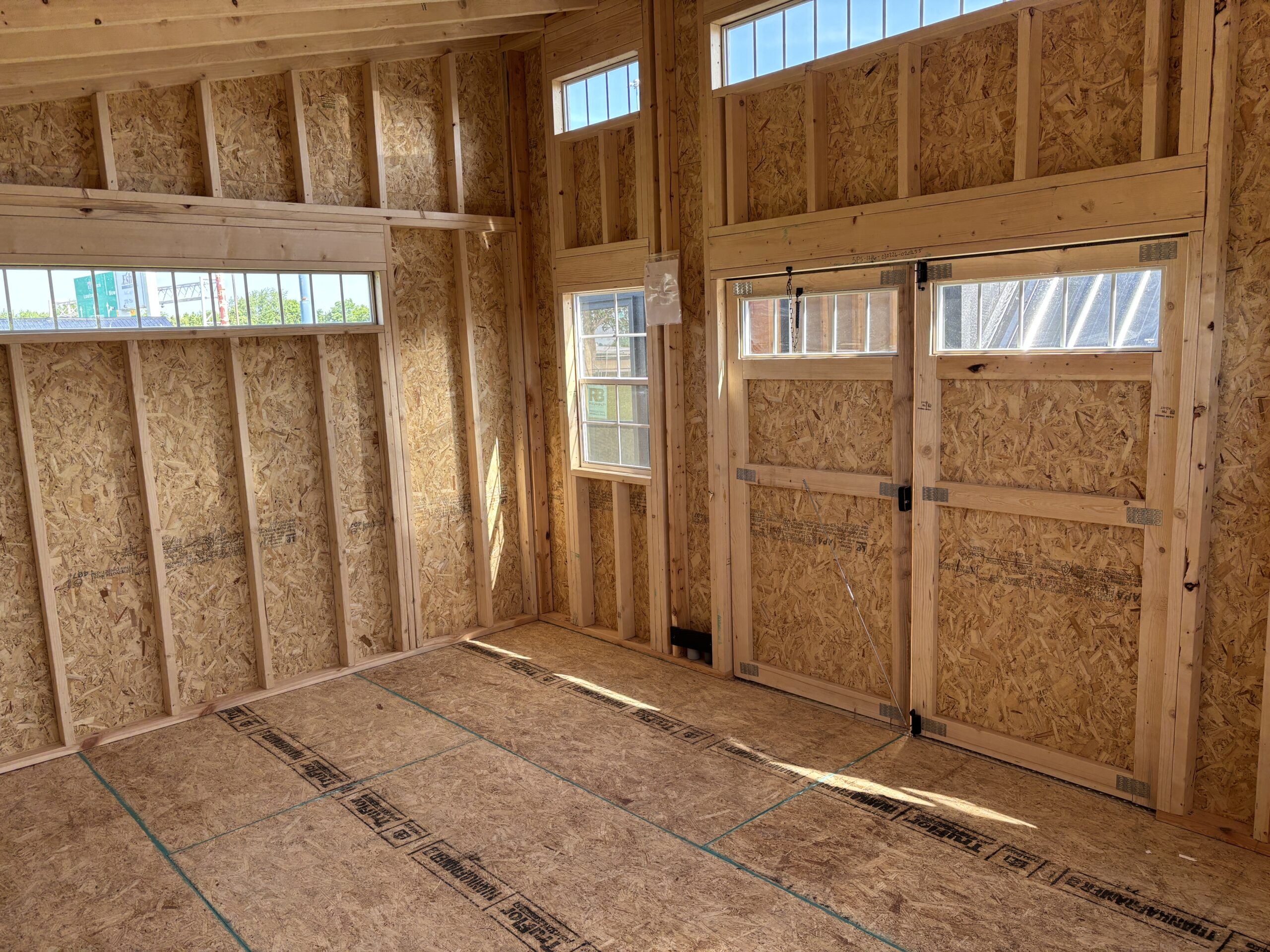 Interior of a wood-framed room under construction with OSB walls, exposed studs, and several windows letting in daylight