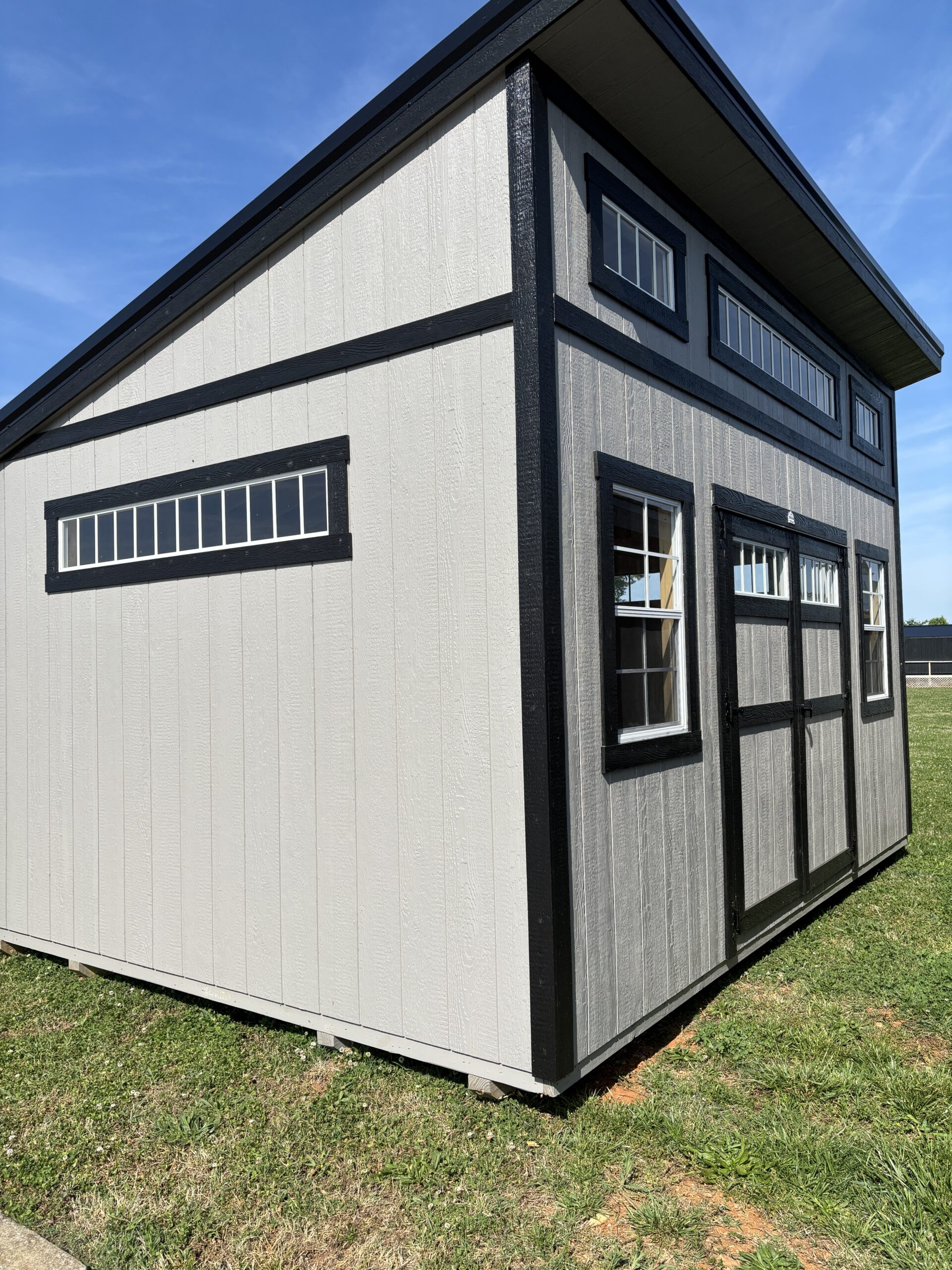 Gray storage shed with black trim and multiple rectangular windows on a grassy lot
