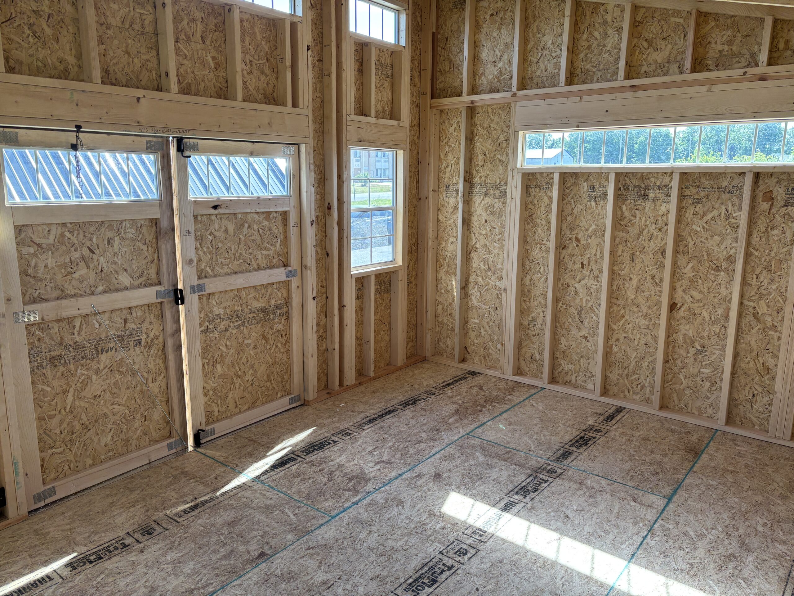 Interior of an unfinished wooden-framed room with OSB walls and multiple windows letting in sunlight