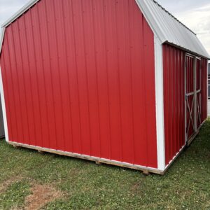 Red metal shed with white trim, angled roof, on a grassy lot under a cloudy sky.