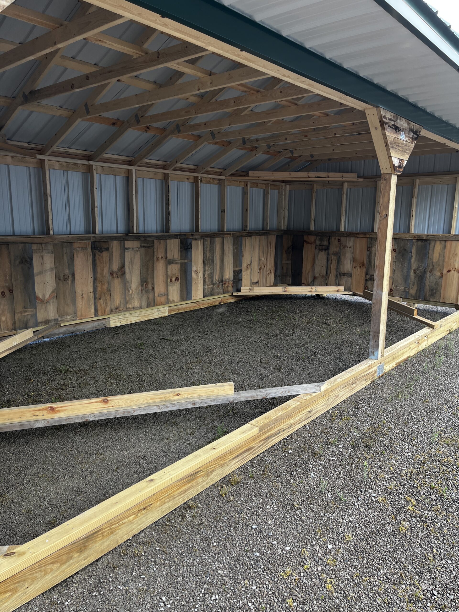 Interior of a partially built wooden shed with metal roofing and exposed framing pieces on the ground inside.