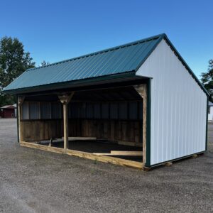 Open-sided wooden shelter with a blue-green corrugated metal roof in a gravel lot under a clear blue sky, with trees in the background.