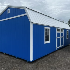 Blue portable storage shed with white trim and a metal roof on a gravel lot, featuring windows and double doors on the side.