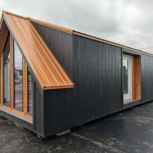 Modern tiny house with black siding, orange metal pitched roof, and large glass wall on the left.